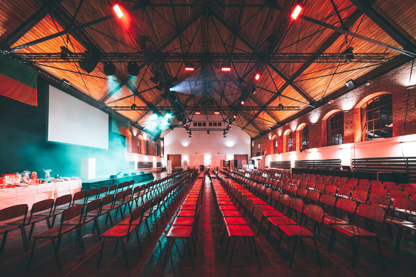 Stimmungsvoll beleuchtete Veranstaltungshalle mit Reihenbestuhlung, großer Leinwand und Bühne in der Phoenixhalle im Römerkastell.