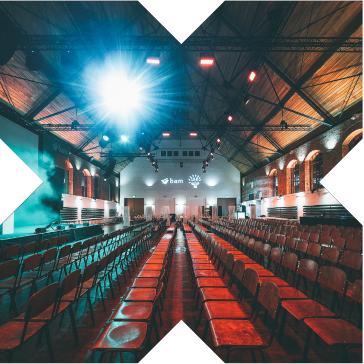 Stimmungsvoll beleuchteter Veranstaltungssaal mit Reihenbestuhlung, großer Leinwand und Bühne in der Phoenixhalle im Römerkastell.