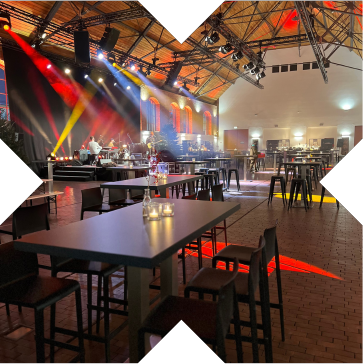 Stimmungsvoll beleuchtete Phoenixhalle im Römerkastell Stuttgart während einer Weihnachtsfeier mit festlich gedeckten Stehtischen und bunter Bühnenbeleuchtung.